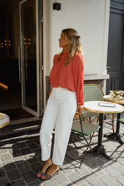 Blouse froncée à col montant terracotta portée par une femme, silhouette entière, pantalon blanc, terrasse