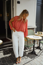 Blouse froncée à col montant terracotta portée par une femme, silhouette entière, mains dans les poches, pantalon blanc