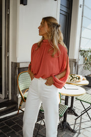 Blouse froncée à col montant terracotta portée par une femme, vue de trois-quarts, pantalon blanc, de côté