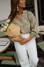 Blouse fleurie légèrement évasée portée par une femme, vue rapprochée, sac beige à la main