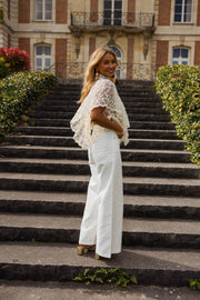 Blouse en dentelle à volants portée par une femme, vue de dos, escalier, pantalon blanc, de loin