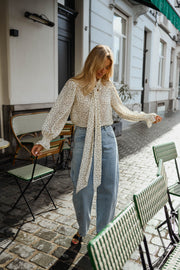 Blouse à pois col lavallière portée par une femme, silhouette entière, jean clair, cardigan blanc ouvert, bras écartés