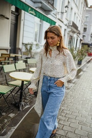 Blouse à pois col lavallière portée par une femme, silhouette entière, jean clair, cardigan blanc ouvert, rue