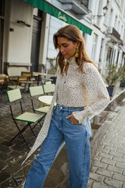 Blouse à pois col lavallière portée par une femme, vue de trois-quarts, jean clair, cardigan blanc ouvert
