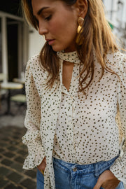 Blouse à pois col lavallière portée par une femme, vue rapprochée, boucles d'oreilles dorées, col lavallière