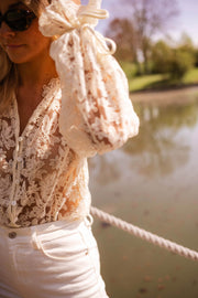 Blouse transparente col V boutonnée écrue portée par une femme, vue rapprochée, manche nouée, lunettes de soleil