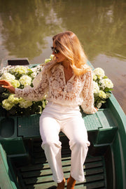 Blouse transparente col V boutonnée écrue portée par une femme, assise, barque verte, hortensias