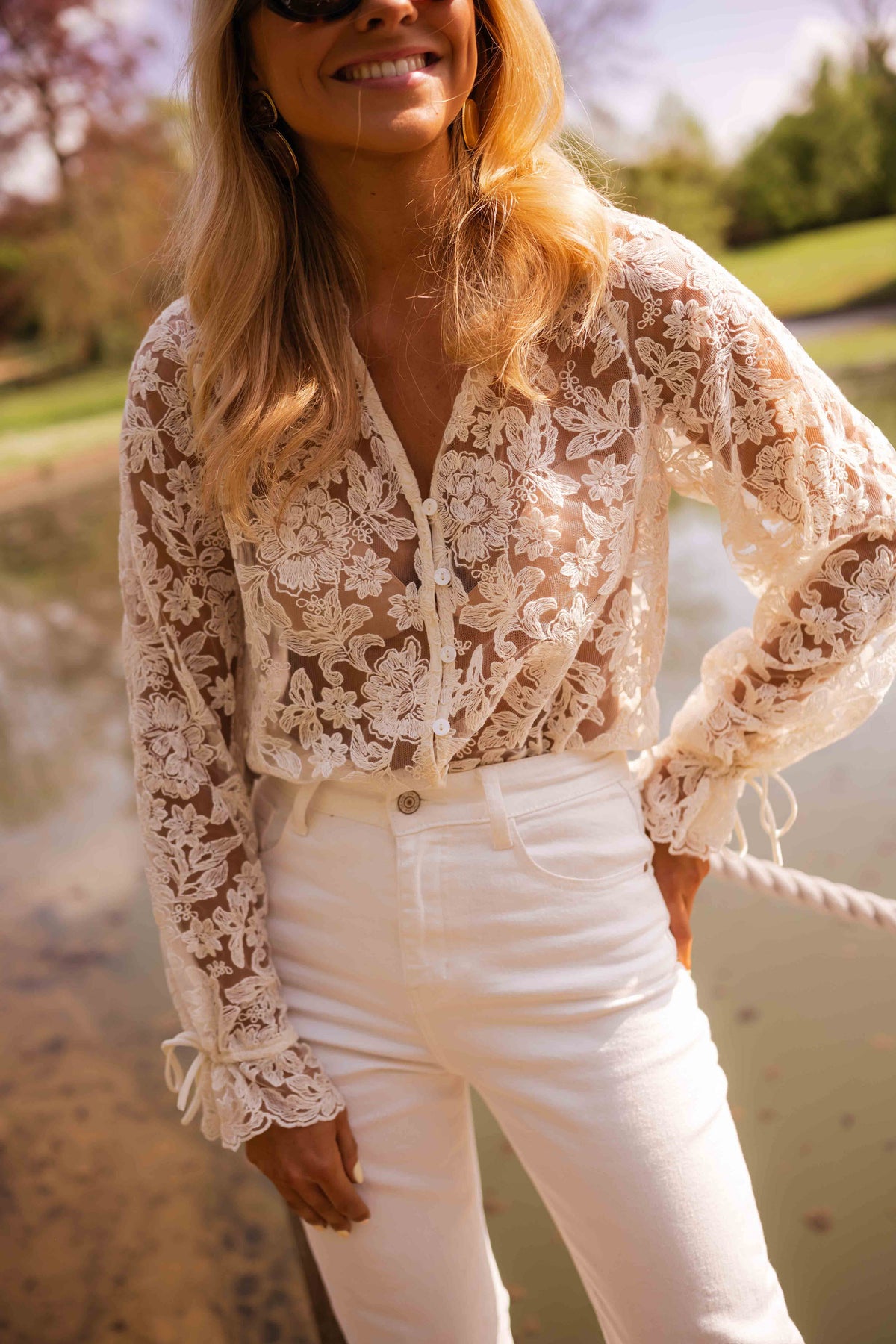 Blouse transparente col V boutonnée écrue portée par une femme, vue de face, étang, pantalon blanc