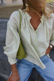Blouse à carreaux manches ballon portée par une femme, vue rapprochée, sac vert à l'épaule