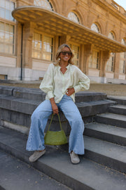 Blouse à carreaux manches ballon portée par une femme, assise, sur des marches, sac vert