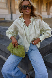Blouse à carreaux manches ballon portée par une femme, vue rapprochée, lunettes de soleil, sac vert