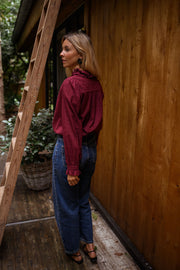 Blouse brodée à col volanté bordeaux portée par une femme, vue de trois-quarts, échelle en bois, cheveux blonds