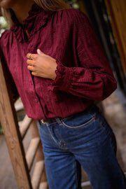 Blouse brodée à col volanté bordeaux portée par une femme, vue rapprochée, blouse bordeaux, mains dans les poches