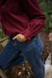 Blouse brodée à col volanté bordeaux portée par une femme, vue rapprochée, manche, main dans la poche