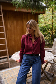 Blouse brodée à col volanté bordeaux portée par une femme, vue de face, terrasse, table blanche