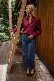 Blouse brodée à col volanté bordeaux portée par une femme, vue de face, échelle en bois, jean large