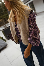 Blouse fluide à col V portée par une femme, vue de trois-quarts, gilet beige, sac bordeaux