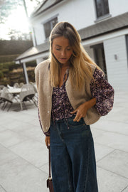 Blouse fluide à col V portée par une femme, vue de trois-quarts, gilet beige, terrasse