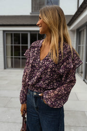 Blouse fluide à col V portée par une femme, vue de trois-quarts, baie vitrée, sac bordeaux