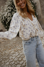 Blouse fleurie fluide à volants portée par une femme, vue de trois-quarts, jean clair, bras tendu