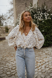 Blouse fleurie fluide à volants portée par une femme, silhouette entière, jean clair, sur des pavés
