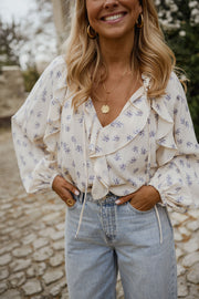 Blouse fleurie fluide à volants portée par une femme, vue rapprochée, cheveux longs, jean clair