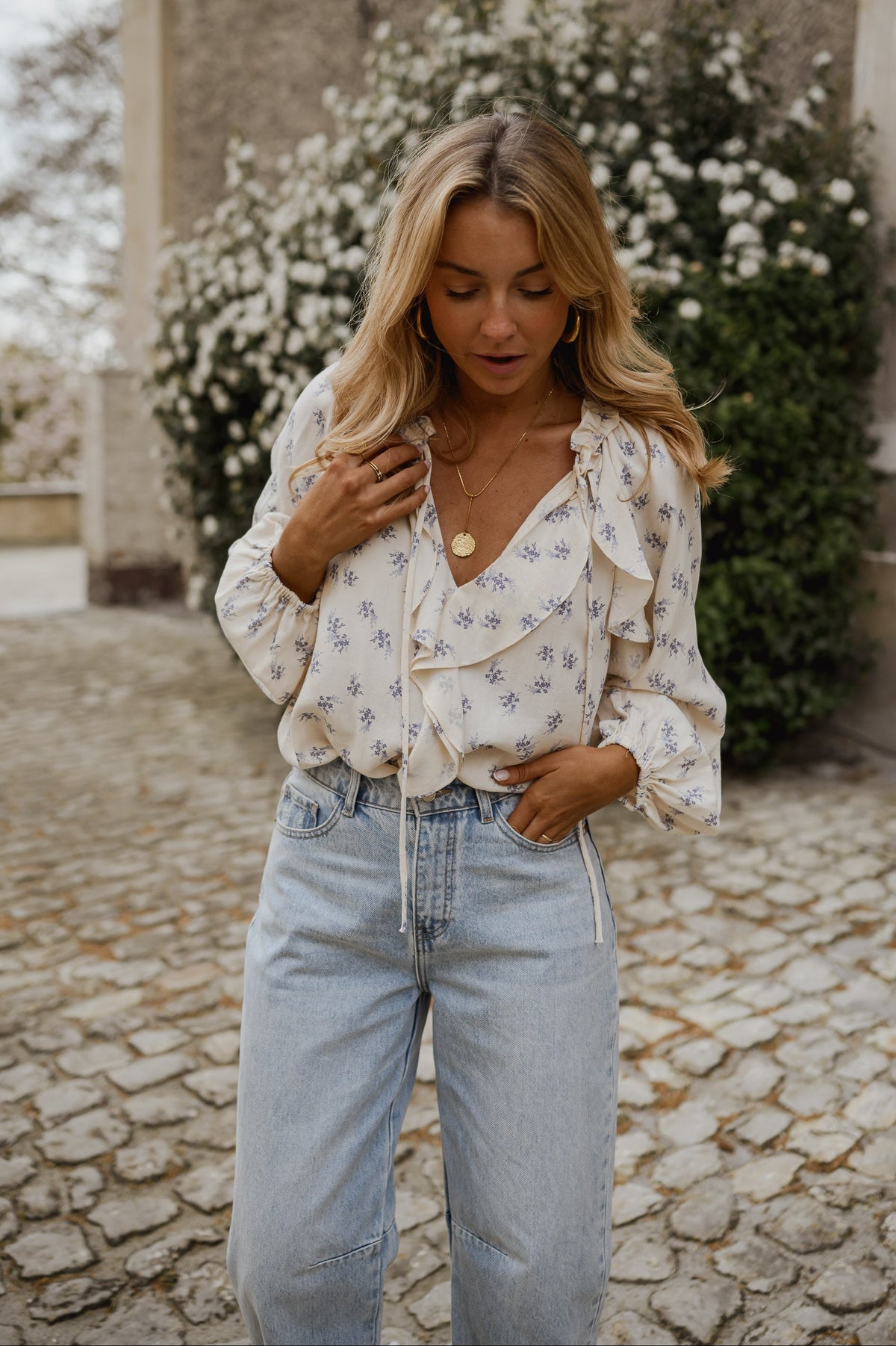 Blouse fleurie fluide à volants portée par une femme, vue rapprochée, mains sur la taille, jean clair