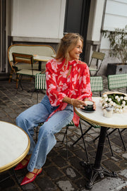 Blouse fluide à col lavallière portée par une femme, assise, sur une chaise, jean clair