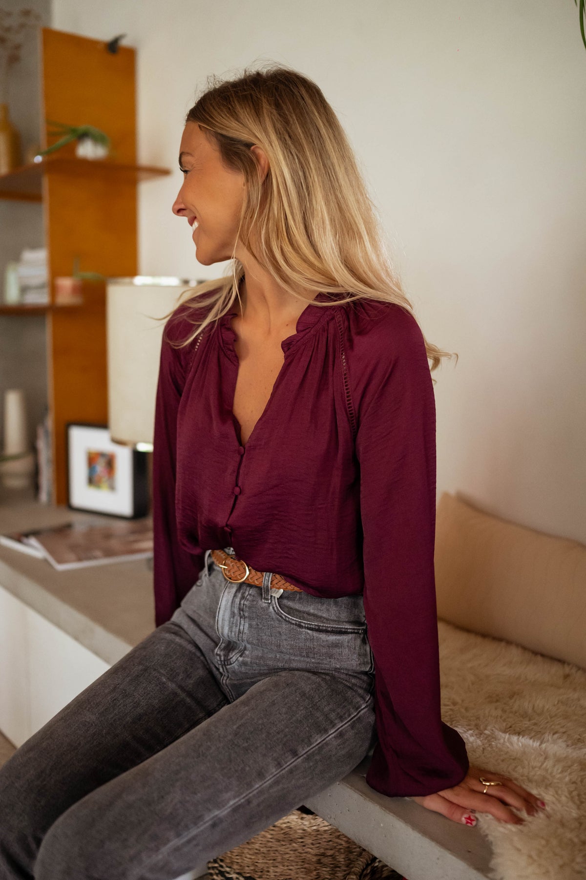 Blouse satinée col V bordeaux portée par une femme, assise, banc, jean gris