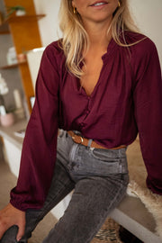 Blouse satinée col V bordeaux portée par une femme, vue rapprochée, col V, ceinture