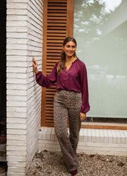 Blouse satinée col V bordeaux portée par une femme, silhouette entière, volets, pantalon léopard