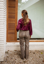 Blouse satinée col V bordeaux portée par une femme, vue de dos, volets, pantalon léopard