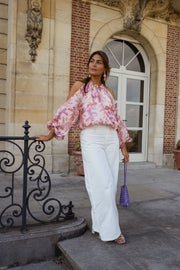 Blouse fleurie à col rond portée par une femme, silhouette entière, grille, pantalon blanc, de face