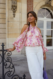 Blouse fleurie à col rond portée par une femme, silhouette entière, pantalon blanc, grille