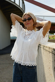 Blouse brodée col montant portée par une femme, vue rapprochée, bras levés, lunettes de soleil