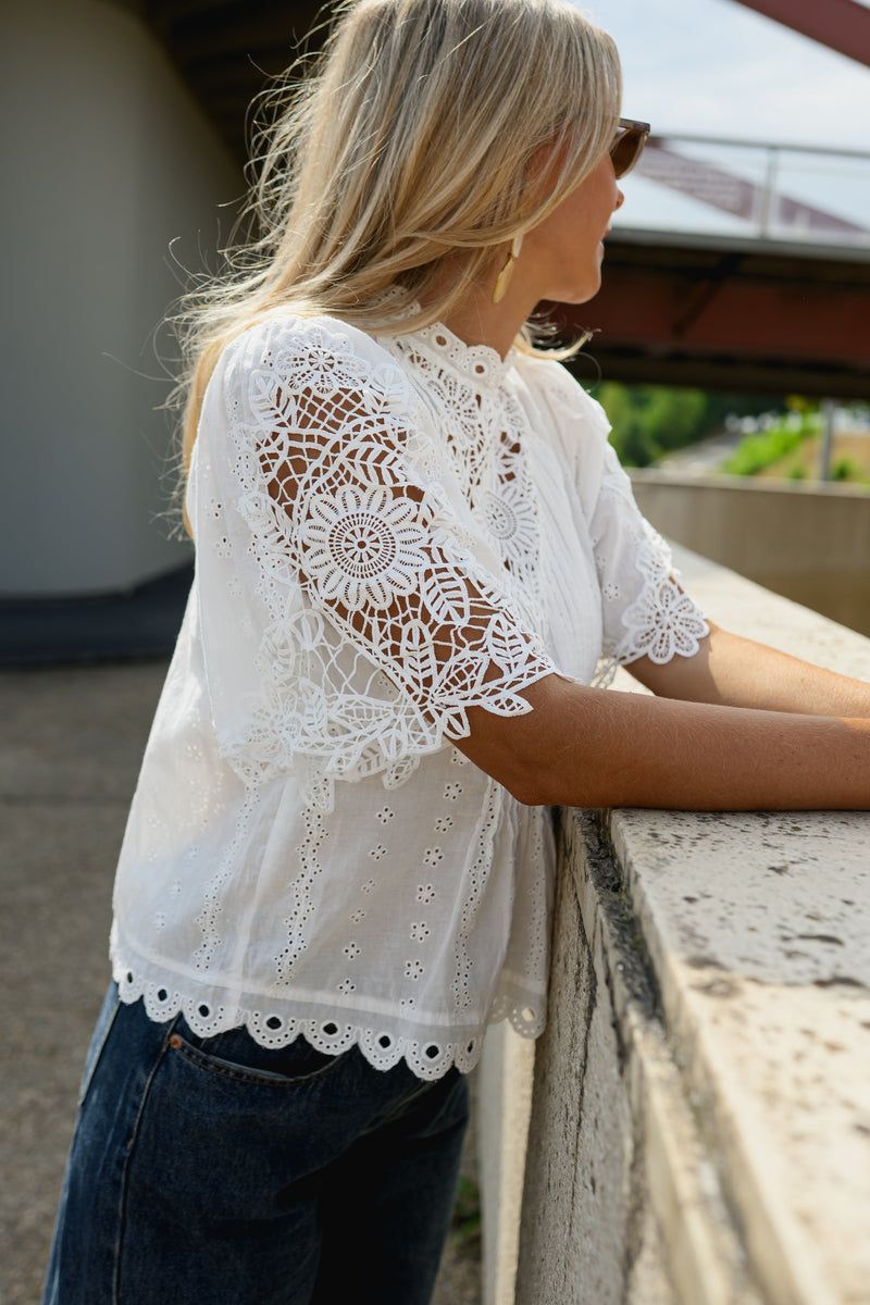 Blouse brodée col montant portée par une femme, vue rapprochée, accoudée à un muret