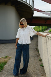 Blouse brodée col montant portée par une femme, en marchant, vue de face, longeant un muret
