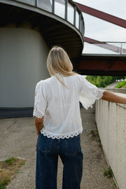 Blouse brodée col montant portée par une femme, vue de dos, devant un muret