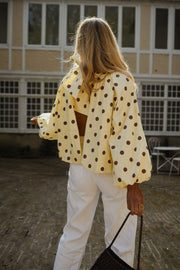 Blouse à pois dos ouvert portée par une femme, vue de trois-quarts, pantalon blanc, sac noir