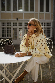 Blouse à pois dos ouvert portée par une femme, assise, à une table, lunettes de soleil