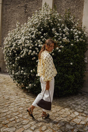 Blouse à pois dos ouvert portée par une femme, vue de dos, devant un buisson fleuri