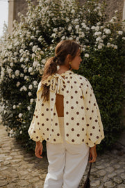 Blouse à pois dos ouvert portée par une femme, vue de dos, dos ouvert, bras le long du corps
