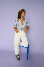Blouse plissée col V portée par une femme, vue de trois-quarts, pied sur un tabouret bleu