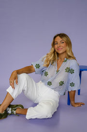 Blouse plissée col V portée par une femme, assise, sur le sol, appuyée sur un bras