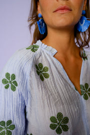 Blouse plissée col V portée par une femme, gros plan de l'encolure et des fleurs vertes