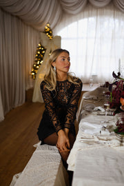 Blouse transparente à perles brodées portée par une femme, assise, table dressée, rideaux blancs