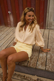 Blouse rayée à manches ballon portée par une femme, assise, short jaune, ponton