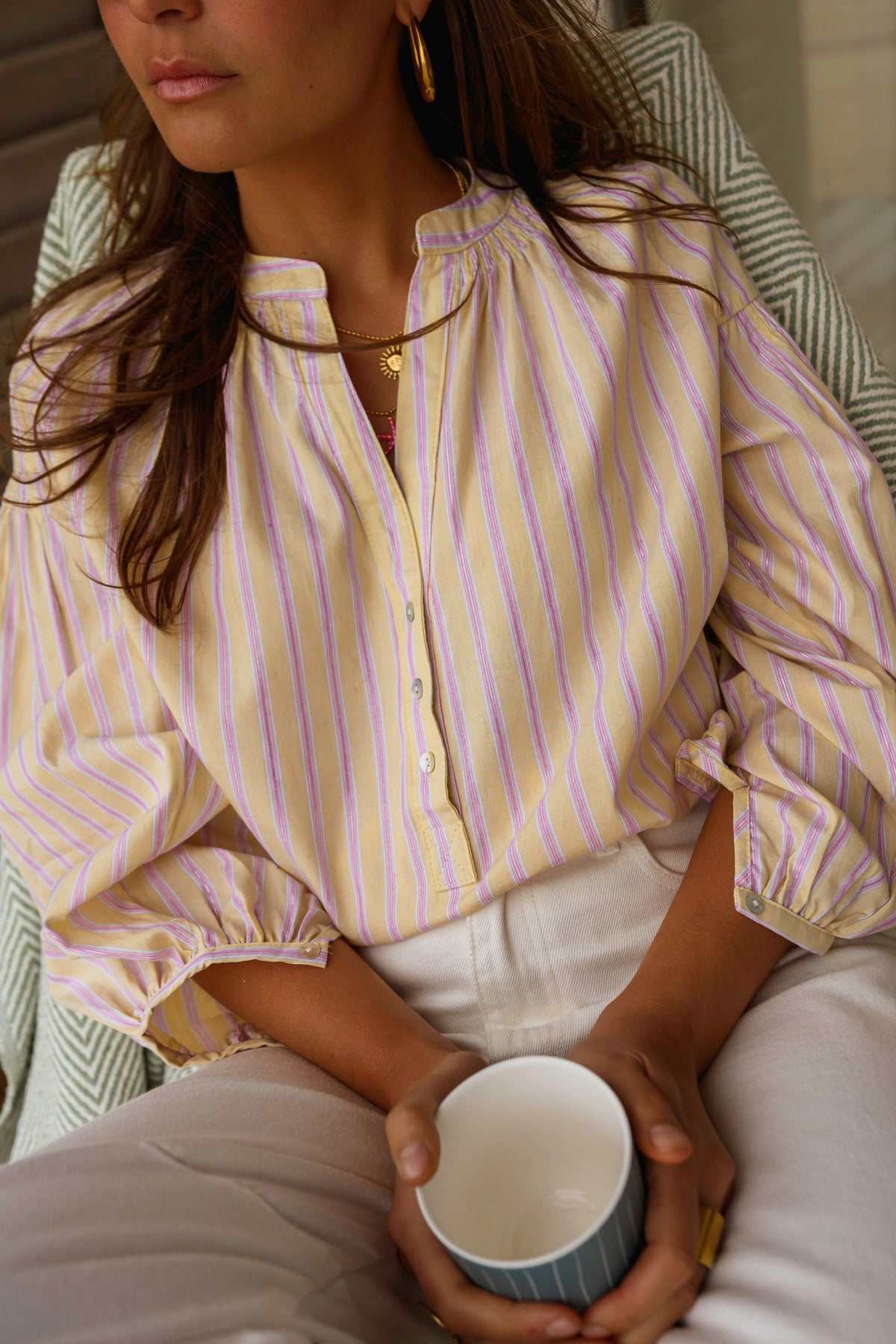 Blouse rayée à manches ballon portée par une femme, vue rapprochée, tasse, pantalon blanc