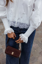Blouse dentelle à col V blanche portée par une femme, gros plan de la dentelle du poignet