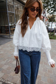 Blouse dentelle à col V blanche portée par une femme, vue de face, sac à main